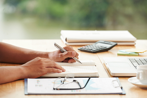 Hands of businessman taking notes in his planner at table