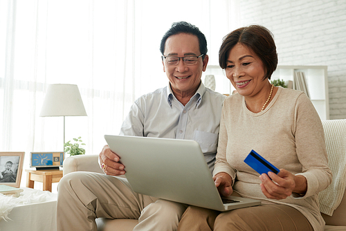 Happy senior Vietnamese couple with laptop and credit card shopping online