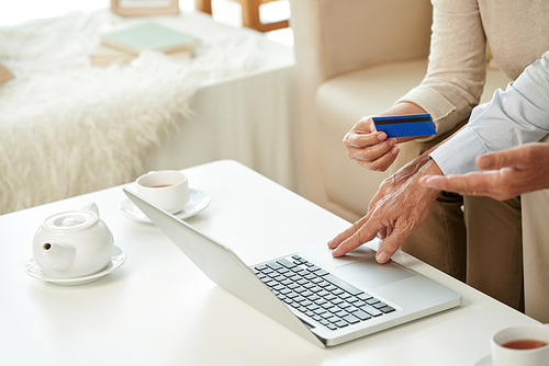 Hands of old couple paying bills online with credit card