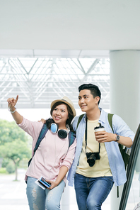 Smiling young woman pointing at something interesting in airport to show her boyfriend