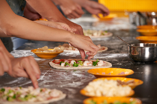Hands of young people making pizzas together
