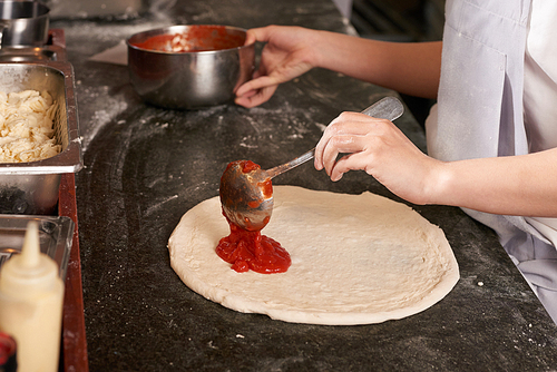 Hands of chef putting classical tomato sauce on pizza base