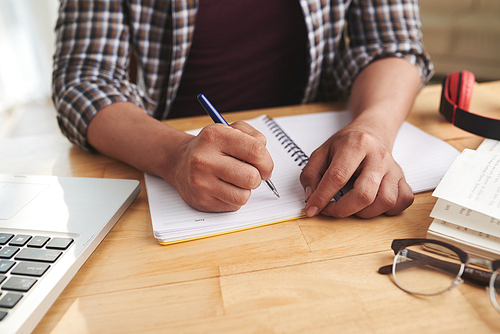 Hands of student writing in textbook at home