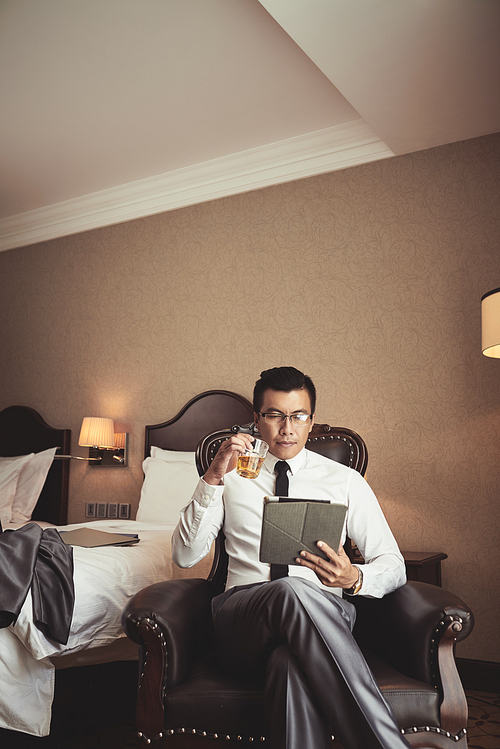 Businessman relaxing after long day with glass of whiskey and digital tablet