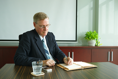 Mature businessman writing plans for the day in notepad