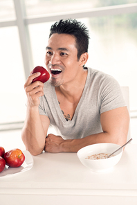 Portrait of Vietnamese young man having cereals and red apple for breakfast