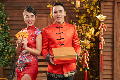 Group portrait of young Asian couple wearing traditional costumes posing for photography with toothy smiles while holding attributes of Vietnamese New Year in hands