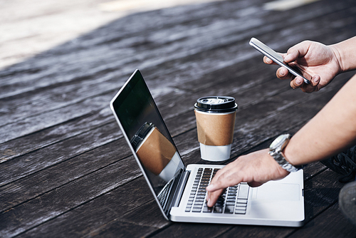 Hands of freelancer working on laptop and checking smartphone