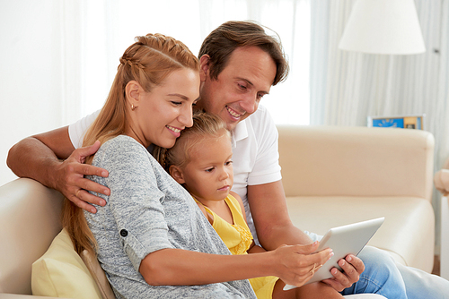 Hugging cheerful family watching cartoons on digital tablet