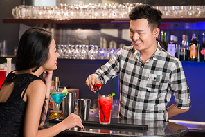 Cheerful bartender making colorful fruit cocktail for pretty woman