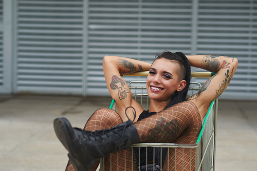 Beautiful smiling young woman with tattooed arms relaxing in shopping cart