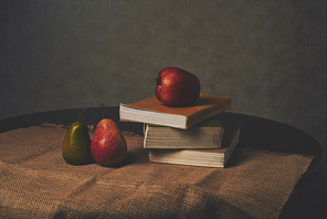 Pears, apple and stack of books on table