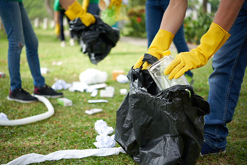 Male hands in yellow rubber gloves putting household waste into small bin bag