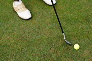 Close-up shot of unrecognizable golfer using club in order to hit ball, green grass of course on background