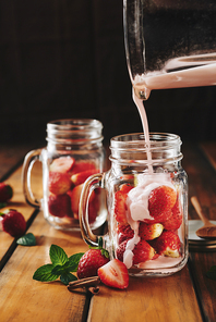 Person pouring yogurt into jar with cut strawberries