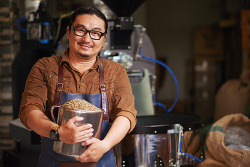 Happy Asian man with big mug on green coffee beans