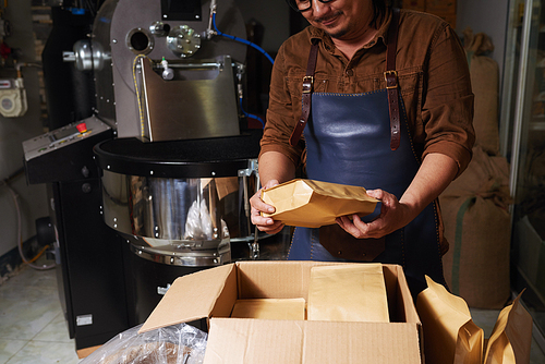 Happy business owner putting packed coffee beans into big box