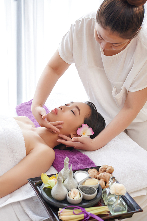 Pretty young woman enjoying face massage while spending weekend in beauty salon, waist-up portrait