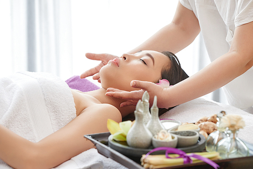 Female beauty therapist preparing skin of her pretty client before applying facial mask, side view