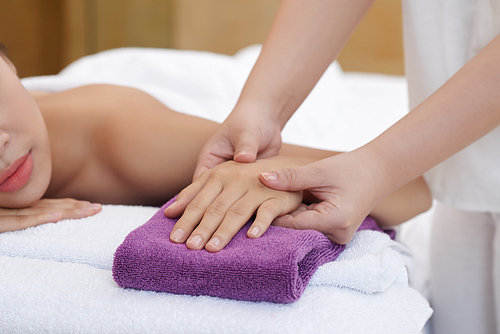 Close-up shot of female hand lying on terry towel and being massaged by therapist in beauty salon