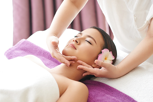 Attractive Vietnamese woman relaxing on massage table during rejuvenation procedure in beauty salon, waist-up portrait