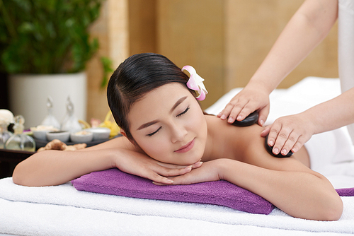 Portrait of calm Asian woman getting hot stone massage in spa center