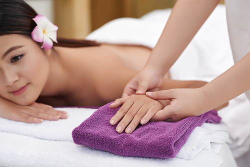 Beautiful Vietnamese woman with flower hair clip enjoying hand massage in beauty salon