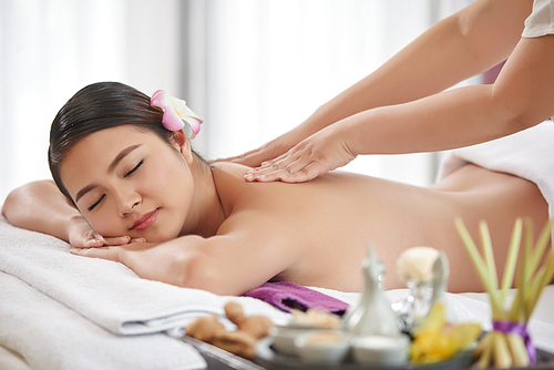 Young Vietnamese woman having nap while being massaged in luxurious spa salon, portrait shot