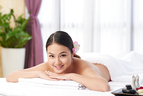 Cheerful pretty Asian woman lying on massage table