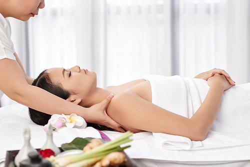 Master massaging shoulders of young woman in spa salon