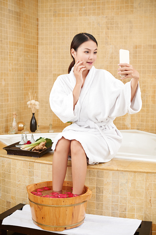 Beautiful young Vietnamese woman taking selfie when having spa procedure