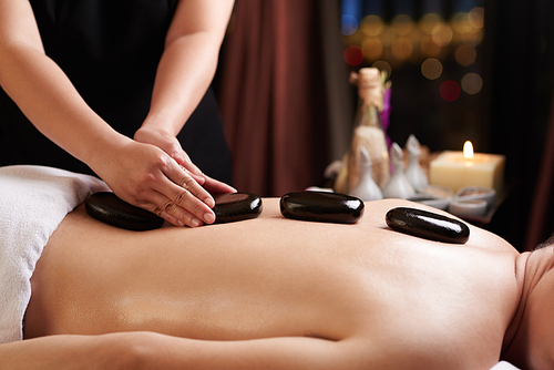 Masseur putting hot stones on the back of young man