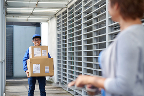 Cheerful young Vietnamese courier carring heavy boxes