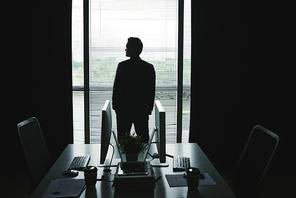 Silhouette of businessman standing at office window and enjoying the view