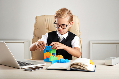 Little businessman playing with colorful bricks at his workplace