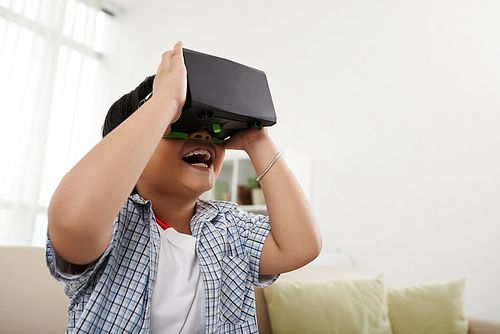 Joyful kid in virtual reality headset playing video game