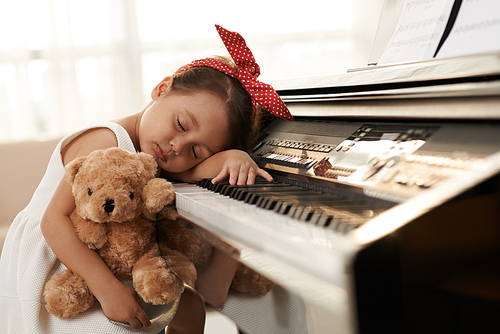 Little girl sleeping on her piano with a toy