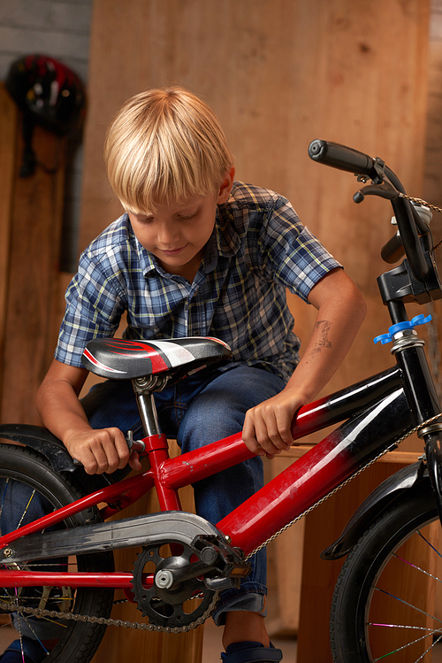 Boy adjusting seat of his bicycle in garage