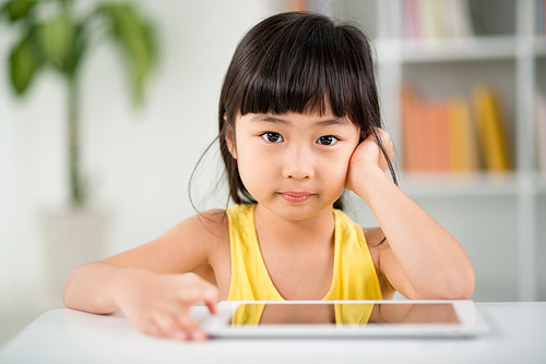 Pretty Vietnamese girl  with deep black eyes while distracted from playing game on digital tablet, blurred background