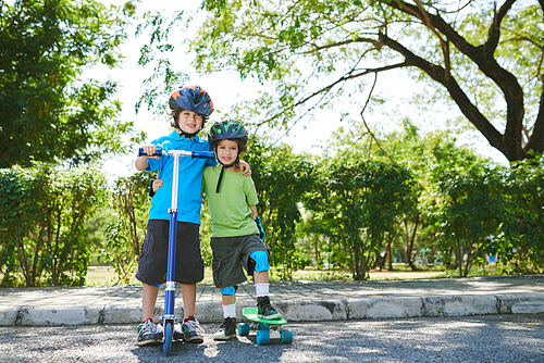 Cheerful little brothers with kick scooter and skateboard