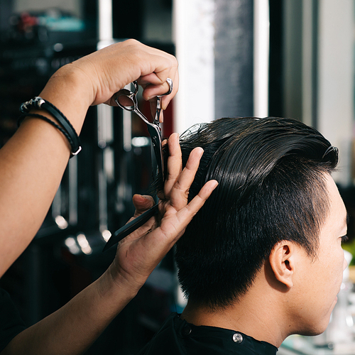Close-up image of barber cutting hair with professional scissors