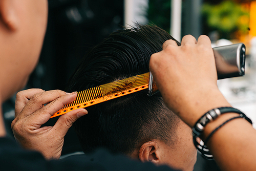 Close-up image of hairdresser using special comb to trim every piece of hair that is too long