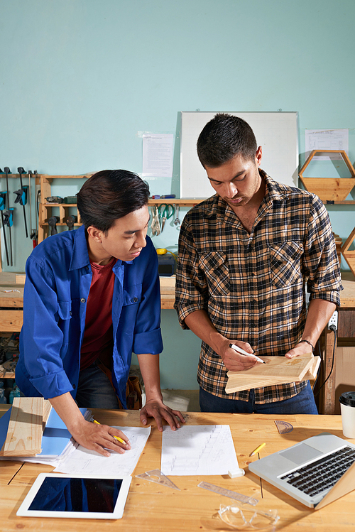 Carpenter explaining work with wood to young apprentice