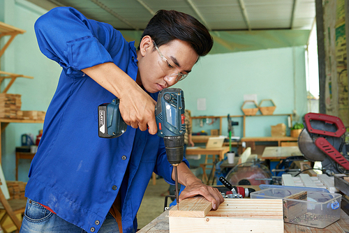 Vietnamese young carpenter driving screws with drill