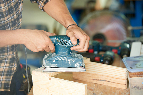 Close-up image of carpenter polishing wooden plank with sanding machine