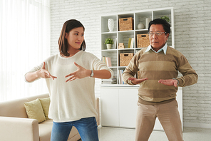 Portrait of pretty young woman and her senior father standing in living room and doing breathing exercises