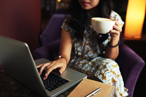Cropped image of young woman drinking morning coffee and checking e-mail