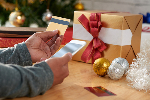 Hands of man using smartphone and credit card to buy Christmas presents