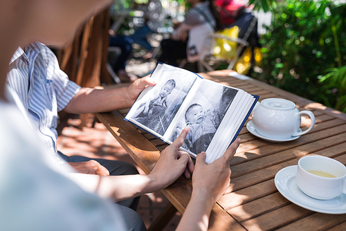 Father and daughter sitting in outdoor cafe and looking at old photos in photo album