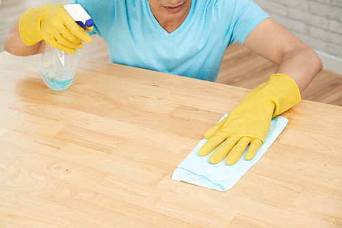 Man spraying and wiping wooden table surface